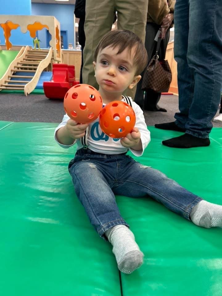 A small kid in jeans holding two small balls