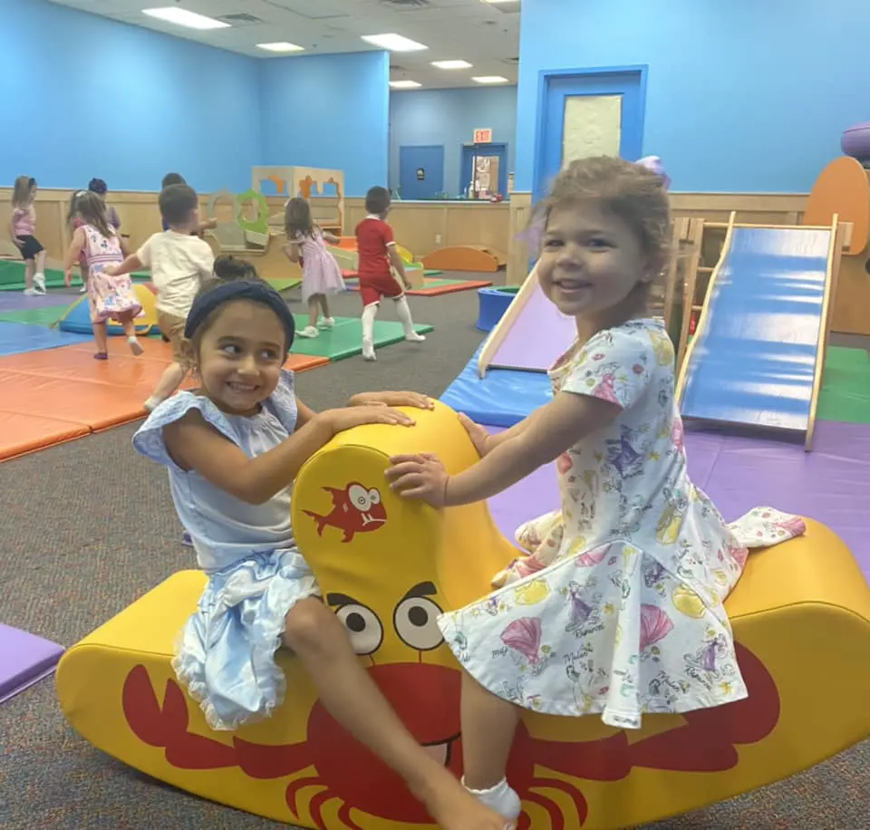 Two girls playing in a small yellow colored see saw